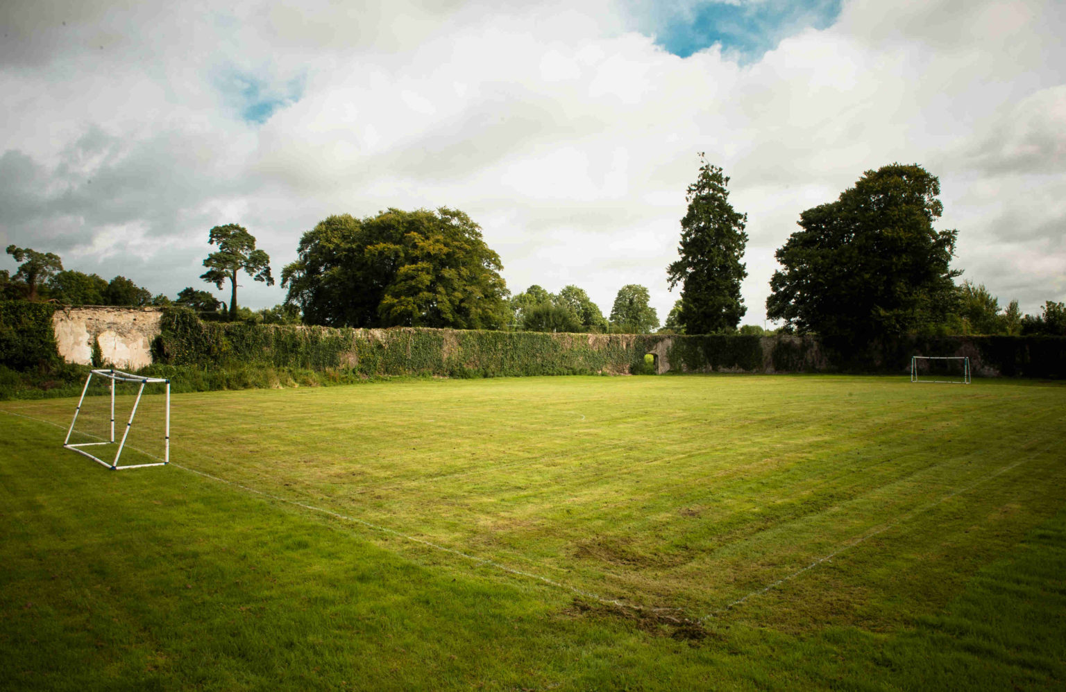 The walled sports field at Castledaly Manor, with goals at either end and an old stone wall behind.